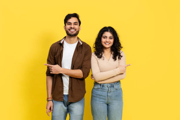 istock Happy Couple Pointing Together Against Yellow Background 2148790112