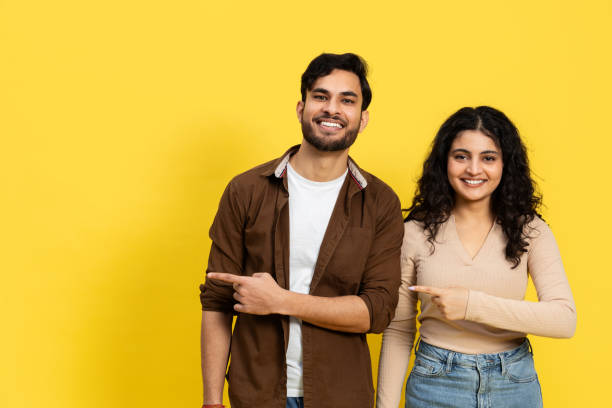 istock Indian Couple Pointing Together Against Yellow Background 2148790120