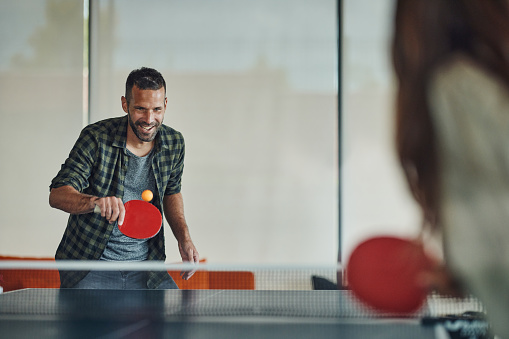 Happy man having fun while playing table tennis with his friend. Copy space.