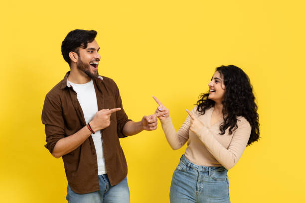 istock Happy Couple Laughing and Pointing Together on Yellow Background 2148790133