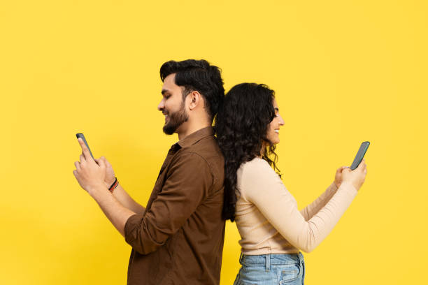 istock Two People Standing Back To Back Using Smartphones On Yellow Background 2148790159