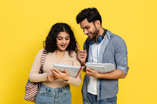 Happy Students Sharing Notes Against Yellow Background