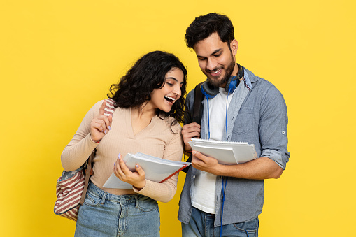 Happy Students Sharing Notes Against Yellow Background