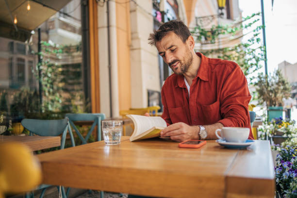 istock Young bearded guy having coffee break while reading a book in outside cafeteria 2148791028