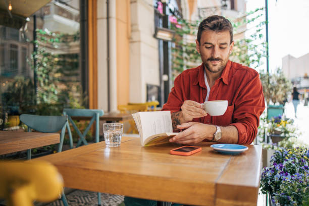 istock Young bearded guy having coffee break while reading a book in outside cafeteria 2148791098