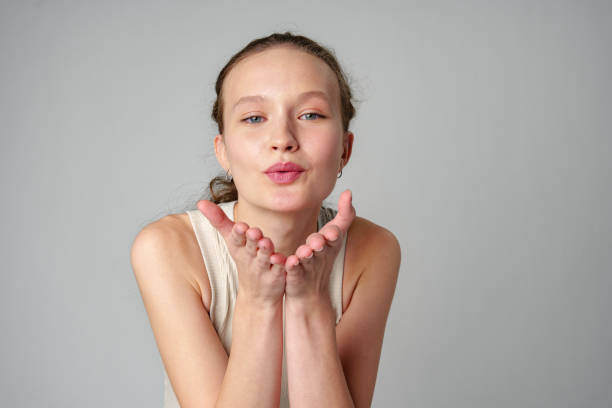 A young blonde woman smiles playfully while blowing a kiss in a stylish studio. Her cheerful demeanor and fashion sense highlight her individuality and confidence.