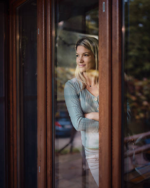 istock Young smiling woman looking through window from her home. 2148791947