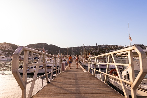 Puerto Andratx, Spain -April 14, 2024:  A pedestrian pier at Puerto Andratx harbor leading to a boat dock. The harbor in Puerto Andratx, Mallorca, is renowned for its affluent international visitors, whether tourists or residents, especially during sunset and for its pub nightlife.