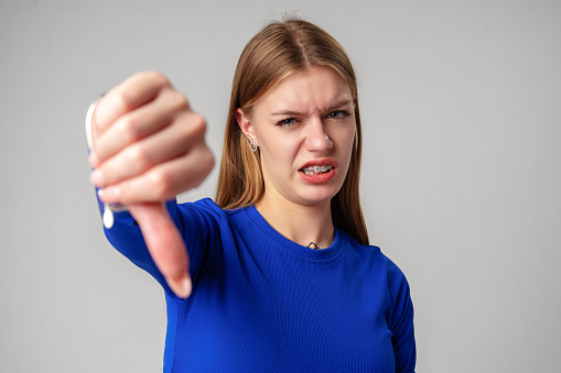 Young Woman Pointing Finger Down at Camera in studio thumb down