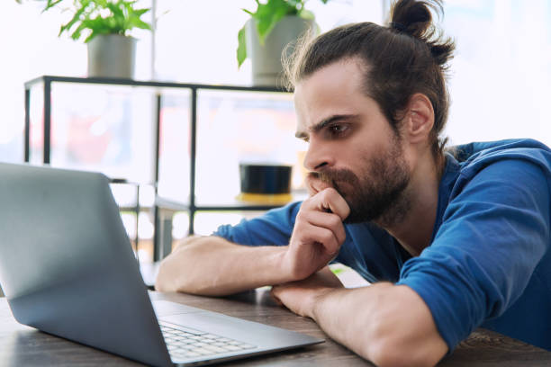 istock Serious tired young man looking at laptop screen 2148792882