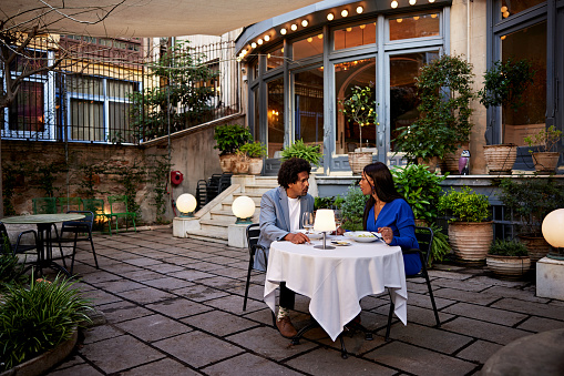 Full length view of man and woman seated outdoors on restaurant patio, face to face and talking.