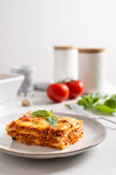 Tomato and ground beef lasagne with cheese and tomatoes layered between sheets of traditional Italian pasta served on a gray plate. Italian menu recipe. Side view, copy space. Tasty homemade lasagna