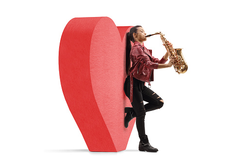 Full length profile shot of a young female saxophonist leaning on a red heart isolated on white background