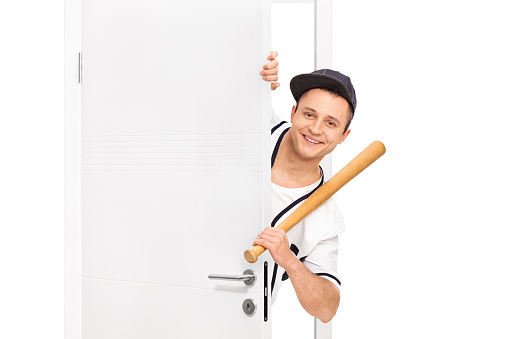 Guy holding baseball bat behind a door isolated on white background