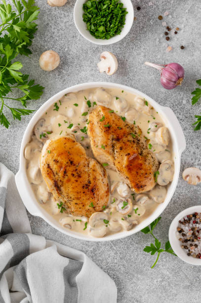 istock Roasted chicken breast with mushrooms in cream sauce on a white ceramic form on a gray concrete background. Comfort food. Top view. 2148795337