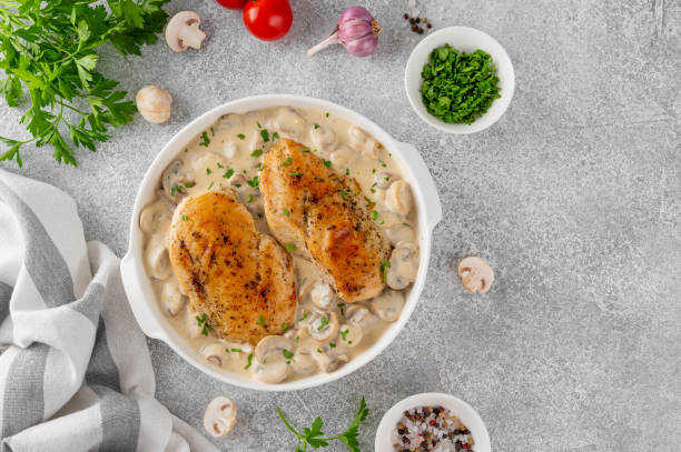 istock Roasted chicken breast with mushrooms in cream sauce on a white ceramic form on a gray concrete background. Comfort food. Top view. 2148795368