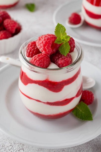 Elegant layered cheesecake featuring smooth white chocolate cream base, decorated with fresh vibrant raspberries and geometric dark chocolate triangles speckled with gold leaf. Sophisticated dessert presentation showcasing multiple cake slices with creamy texture and professional bakery styling. Perfect for upscale celebrations, gourmet food photography, and premium confectionery marketing.