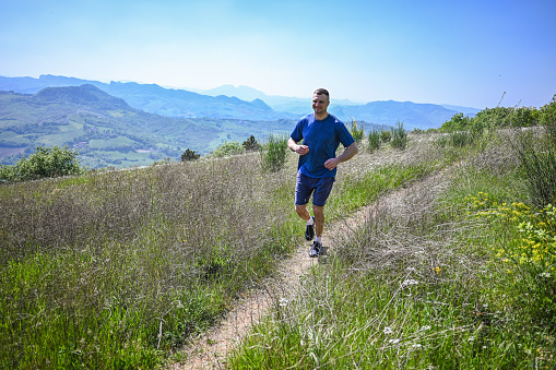 Young sportsman running on meadow in mountains.