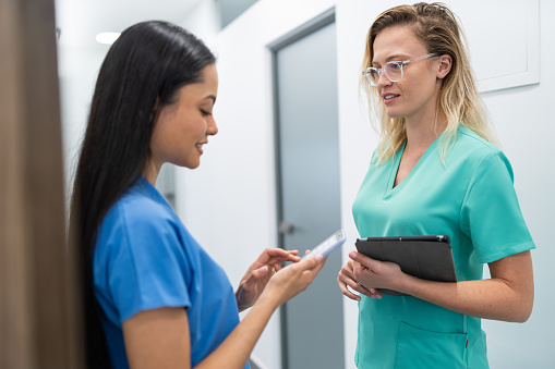 Two female dental workers in uniform, standing in hallway in modern dental clinic discussing the upcoming tasks for the day
