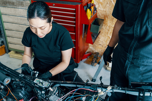 Mid adult male and female mechanics repairing a motorcycle in a small business garage