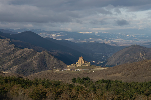 Jvari Monastery from the mountain in the east early in the morning. Part of the city of Mtskheta is visible. Snowy mountains, sky and clouds in the background
