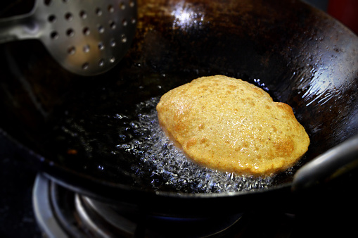 One Poori - Deep fried Indian flatbread or puri made of wheat flour popular in India being cooked deep fried in very hot fuming cooking oil in. a kadaai or cooking pan or wok