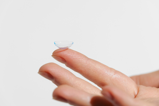 Finger of female hand holding blue transparent contact lens on white isolated background. Concept of ophthalmology, myopia, treatment of disorders, medicine.