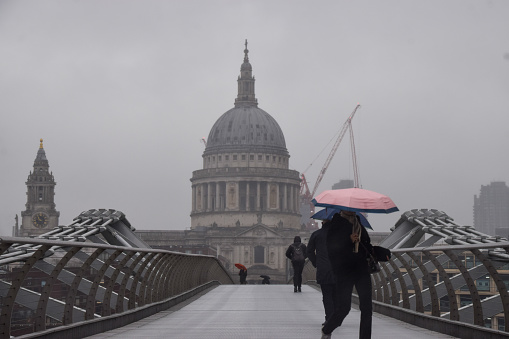 London, UK - February 8 2024:  People walk with umbrellas along Millennium Bridge past St Paul's Cathedral on a rainy day.