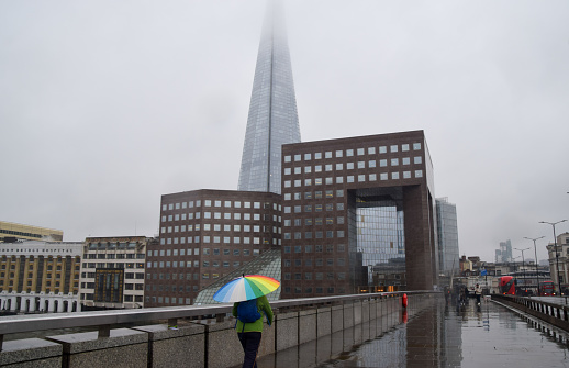 London, UK - February 8 2024:  A person walks with a colourful umbrella along London Bridge past the Shard building on a rainy day.