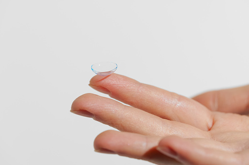 Finger of female hand holding blue transparent contact lens on white isolated background. Vision improvement concept, ophthalmology, myopia.