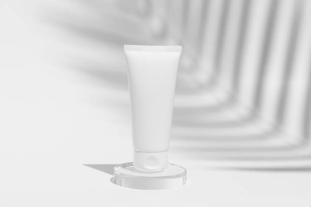 istock White face cream tube mockup on glass on white isolated background with shadow from palm tree. Natural cosmetics for skin care. 2148802666