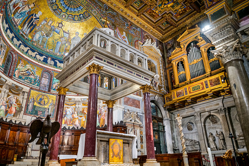 A splendid view of the mosaics decorating the apse inside the ancient Basilica of Santa Maria in Trastevere (Our Lady in Trastevere), in the historic heart of Rome. In the centre, in the foreground, the marble tabernacle and the main altar, while on the right the organ built by Filippo Testa in 1702. This Romanesque-style basilica, founded by Pope Callixtus I around 220 AD, is one of the oldest churches in Rome. In the upper part of the apse a 12th century mosaic depicts the Virgin and Christ seated on the same throne, while the mosaics in the lower part of the apse depict the life of the Virgin Mary, by the medieval artist Pietro Cavallini (1259–1330). Trastevere is an iconic district of the Eternal City, due to the presence of countless artistic and historical treasures, monuments and ancient Romanesque and Baroque churches, but also for its squares and alleys to be explored freely, where it is easy to find typical restaurants, pubs, small shops of artisans and scenes of daily life with the original Roman soul. In 1980 the historic center of Rome was declared a World Heritage Site by Unesco. Wide angle image in high definition quality.