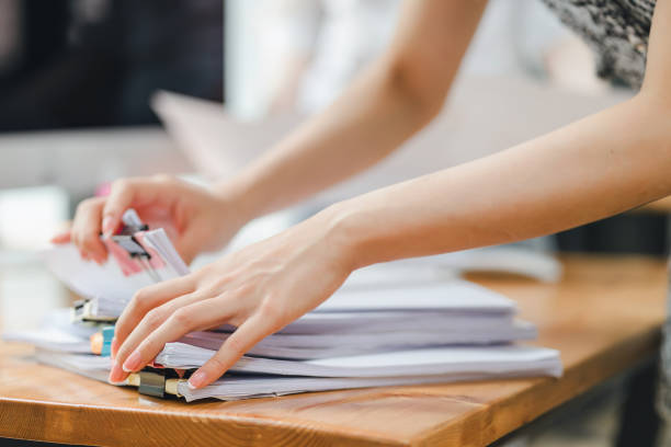 istock Close-up of hands organizing a stack of documents with colorful binder clips on a wooden table. 2148804481