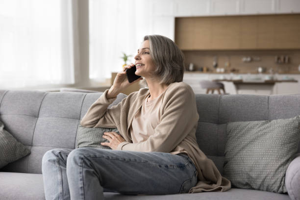 istock Positive mature woman sitting on sofa talking on mobile phone 2148804944