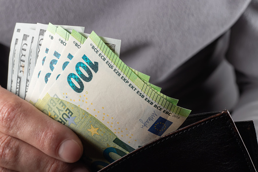 Man handing wallet with 100 euro and 100 dollars banknotes.