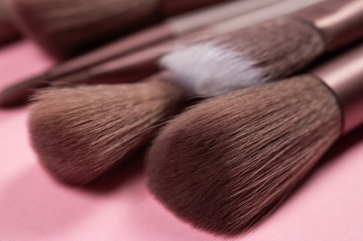 Various makeup brushes over pink background.