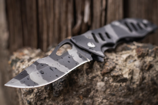 Tactical folding knife with water drops for survival on stone background.