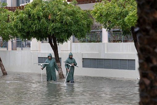 Dubai, United Arab Emirates, 16th April 2024: Two street cleaners trying to unblock the drains on the flooded streets of popular residential area in Dubai after a heavy downpour