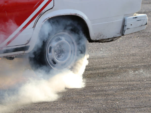 Thick red and white bengal torch smoke rises from a tire during a car drift show, with a person partly hidden in the haze. Selective focus.