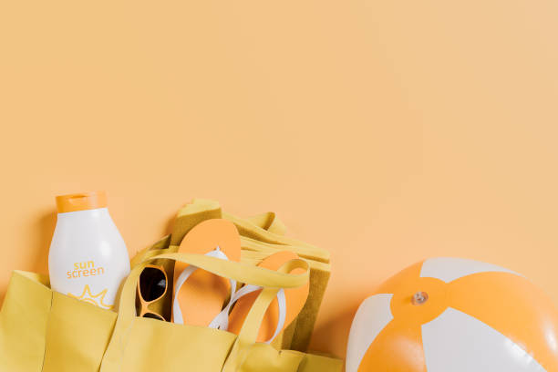 Summer Beach Accessories with Sunscreen and Beach Ball on Orange Background