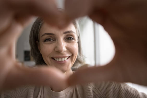 istock Cheerful pretty older woman shows heart gesture looking at camera 2148807702