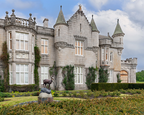 Crathie - United Kingdom. May 26, 2023: A detailed segment of Balmoral Castle exterior, featuring a deer statue amidst its gardens. The castle ivy-clad stonework and architectural elegance are emphasized