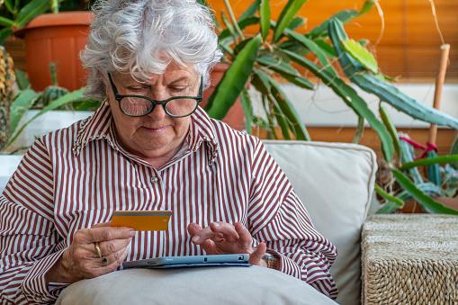 Beautiful elderly adult woman with short grey hair and glasses is sitting on a sofa at home holding an ipad. Portrait of a confident Caucasian female senior grandmother or mother with different facial expressions: happy, worried, thinking, planning, dreaming. Set of 19 photos, close-up.