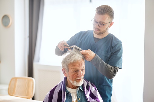 Close-up of a caregiver giving a haircut to a senior man