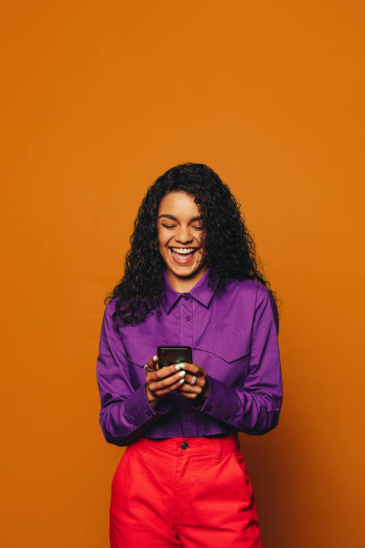istock A vibrant woman texting on a orange background, using a smartphone 2148809719