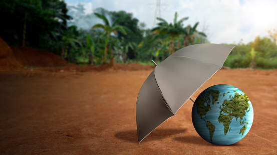 A black umbrella protects the globe on the ground with a blue sky background. Earth day concept