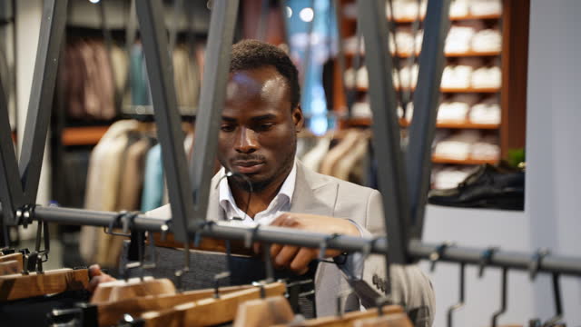 Young man choosing pair of pants in fashion store