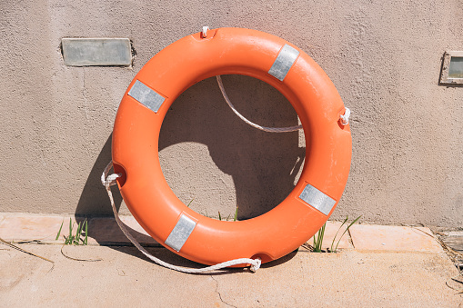 Orange lifesaver ring leaning against the wall near a swimming pool