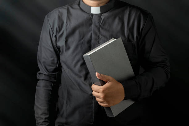 istock Young priest holding bible isolated on black background. 2148814236