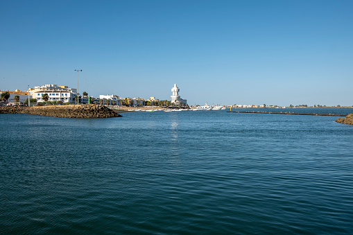 Isla Crisitna, Huelva, Spain - August 13, 2023: The lighthouse, at Isla Cristina and the beach Playa el Cantil, as seen from Punta del Moral, near Ayamonte, Huelva Province, Andalucia, Spain